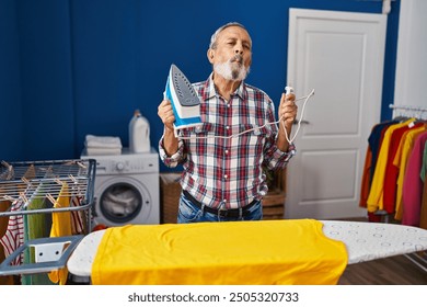 Crazy fun in the laundry room, comical senior man making fish face with iron machine - Powered by Shutterstock