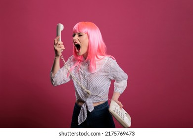 Crazy Funky Person Screaming At Landline Phone Call On Camera, Posing And Talking On Retro Vintage Telephone. Having Remote Conversation With Stationary Cord Phone, Trendy Woman In Studio.