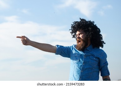 Crazy Funny Bearded Man With Black Wig Pointing Finger On Sky Background. Funny Facial Expressions.