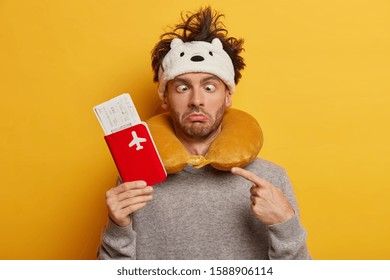 Crazy Funny Passenger Crosses Eyes, Has Messy Hair, Wears Neck Pillow For Comfort During Plane Flight, Points At Passport With Tickets, Isolated On Yellow Wall, Waits In Airport For Delay Flight