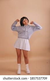 Crazy girl with a bob haircut, in a blue hoodie and white short skirt, having fun on isolated beige background. Anime fan.