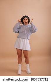 Crazy girl with a bob haircut, in a blue hoodie and white short skirt, having fun on isolated beige background. Anime fan.