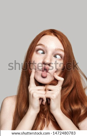 Crazy girl Close up photo of happy young redhead woman making crazy face and grimacing while standing against grey background