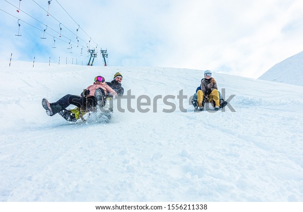Crazy happy friends having fun with sledding on\
snow high mountains - Young millennial people making luge\
competition at white week vacation - Winter sport and travel\
concept - Focus on guys\
faces