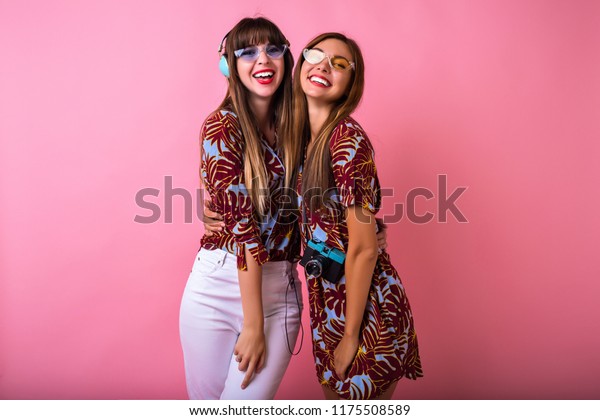 Crazy happy friends sister girls hugs\
end enjoy vintage party, tropical color matching outfits, amazing\
smiles, film camera and headphones, posing on\
camera.