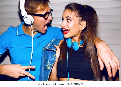 Crazy hipster couple having fun, screaming singing and smiling, looking to each other , having fun at romantic date, listening music at big headphones, trendy bright clothes.