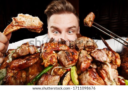 Crazy hungry man eating mix grill meat. Emotional content for restaurant promo. Cheat day. Meat lover. Lamb chops, chicken tikka, kebab, lamb, beef steak. 