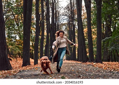 Crazy jogging with a dog in the autumn park. A young beautiful woman runs with a purebred dog that pulls on a leash and laughs.