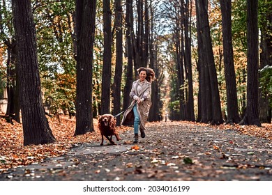 Crazy jogging with a dog in the autumn park. Woman running in the park with a dog on a leash with joyful emotions and pleasure.