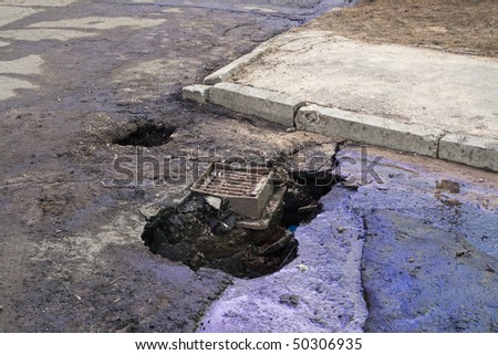 Crazy Latvian roads series: huge potholes in asphalt near manhole with poured oil.