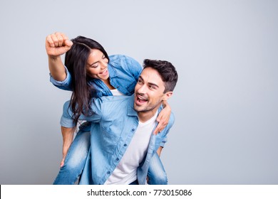 Crazy lovely lovers celebrating a victory, looking to each other, woman raised her hand with fist up in piggy back style over grey background