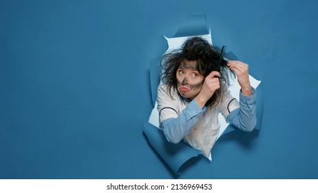 Crazy Mad Chemist With Messy Hair After Explosion Using Comb To Make Funny Goofy Hairstyle In Studio. Amusing Insane Scientist Using Brush And Doing Silly Foolish Facial Expressions.