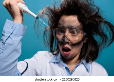 Crazy mad chemistry reasearcher with dirty face and messy hair experimenting with unknown compounds. Lunatic chemist looking shocked at professional pipette filled with experimental liquid substance.