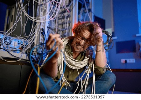 Crazy mad computer engineer wrapped in wires and cables in server room