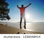 Crazy man jumping while joogging at morning spring lake bay. Sunny morning with clear blue sky above.