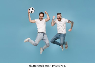 Crazy men guys friends in white t-shirt isolated on pastel blue background. Sport leisure lifestyle concept. Cheer up support favorite team with ball, jumping doing winner gesture, screaming celebrate