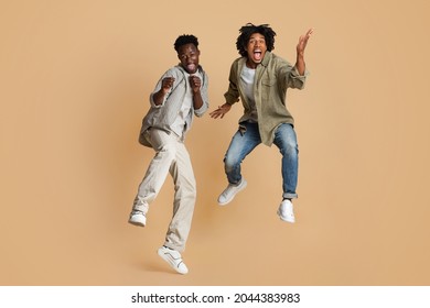 Crazy Mood. Two Overjoyed Black Guys Jumping Over Beige Studio Background, Full Length Shot Of Happy Emotional African American Male Friends In Casual Clothes Having Fun Together, Copy Space