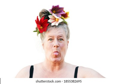 Crazy Older Woman With Gray Hair And Colorful Flowers In Her Updo Hairstyle Sticks Her Tongue Out Against A White Background                                
