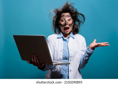 Crazy Panicked Scientist Screaming In Panic After Laboratory Explosion While Having Laptop. Insane And Scared Chemist With Dirty Face And Messy Hair Yelling In Fright After Failed Chemical Experiment.