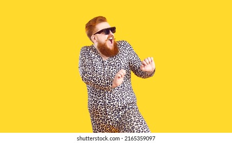 Crazy Plus Size Man In Funny Pajamas Dancing And Having Fun In Fashion Studio. Happy Bearded Fat Guy Wearing Cool Sunglasses And Comfy Leopard PJs Singing And Dancing Isolated On Yellow Background