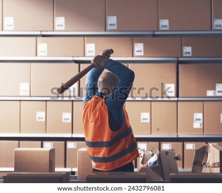 Crazy rebellious warehouse worker smashing cardboard boxes with a baseball bat