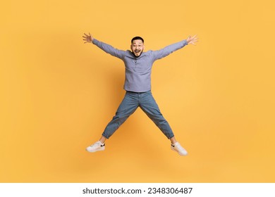 Crazy Sales. Funny Asian Man Jumping Like A Star Over Yellow Background, Carefree Millennial Guy Spreading Arms And Legs And Looking At Camera, Fooling And Having Fun, Full Length With Copy Space