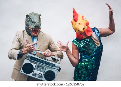 Crazy senior couple dancing for new year's eve party wearing t-rex and chicken mask - Old trendy people having fun listening music with boombox stereo - Absurd and funny trend concept - Focus on faces