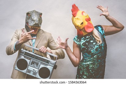 Crazy senior couple wearing chicken and t-rex mask while dancing outdoor - Mature trendy people having fun celebrating and listening music with boombox - Absurd concept of masquerade funny holidays