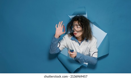 Crazy Silly Scientist Grinning And Showing Test Tubes On Camera, Doing Foolish Mad Facial Expressions. Goofy Sunny Woman Acting Insane And Amusing, Having Messy Insane Hair In Studio.