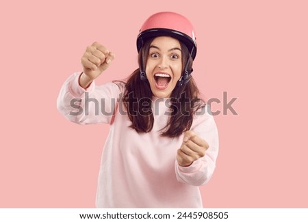 Crazy smiling amazed woman with opened mouth in helmet imagines she is driving and holding steering wheel on pink background. She is wearing pink sweatshirt. Human emotions, energy, drive concept.