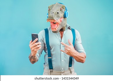 Crazy tattooed man with t-rex mask using smartphone while listening music - Crazy senior male having fun with mobile phone app - Technology trends and fashion concept - Focus on face - Powered by Shutterstock