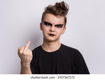 Crazy Teen Boy With Spooking Make-up Making Of Punk Goth Dressed In Black, Showing Middle Finger On Gray Background. Problems Of Transitional Age