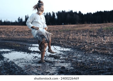 Crazy woman dancing barefoot and splashing in a puddle of mud in a field, freedom concept