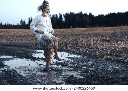 Crazy woman dancing barefoot and splashing in a puddle of mud in a field, freedom concept