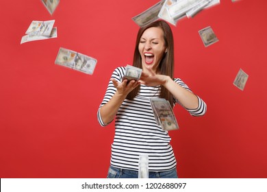 Crazy woman in striped clothes screaming scattering throwing out money banknotes lots of dollars isolated on bright red wall background. People sincere emotions, lifestyle concept. Mock up copy space