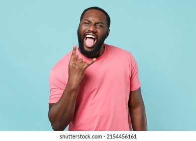 Crazy young african american man 20s in casual pink t-shirt isolated on blue background studio portrait. People lifestyle concept. Mock up copy space. Depicting heavy metal rock sign horns up gesture