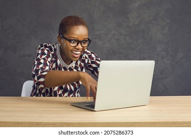 Crazy Young Black Woman In Glasses Sitting At Desk With Laptop Computer, Typing In Information And Looking At Screen With Funny Happy Face Expression