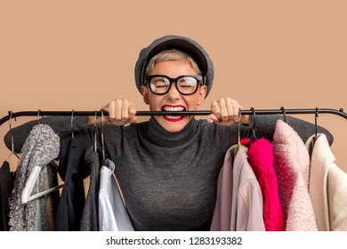 Crazy Young Girl With Fair Hair Is Trying A Wordrobe. Playful Angry Woman In Hat Is Biting Hangers While Shopping . Tiredness After Shopping. Bad Shopping Day. Emotions