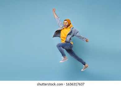 Crazy young hipster guy in fashion jeans denim clothes posing isolated on pastel blue background. People lifestyle concept. Mock up copy space. Jumping, spreading hands, clenching fists like winner - Shutterstock ID 1636317637