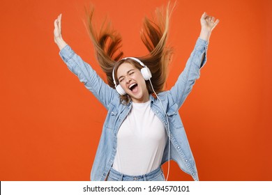 Crazy Young Woman Girl In Casual Denim Clothes Posing Isolated On Orange Background. People Lifestyle Concept. Mock Up Copy Space. Listen Music With Headphones, Rising Hands Up, Dancing Screaming