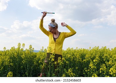crazy young woman posing in beautiful big yellow blooming rapeseed or oilseed rape field. girl holding musicalinstrument called flute or whistle. spring nature wallpaper. farming.