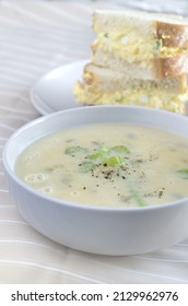 Cream Of Celery Soup In A White Bowl With Blurred Egg Salad Sandwich In Background Vertical