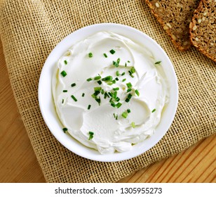 Cream Cheese, Quark Or Yogurt In A White Bowl. Dairy Product With Fresh Herbs, Healthy Eating Theme. Wooden Table Background.