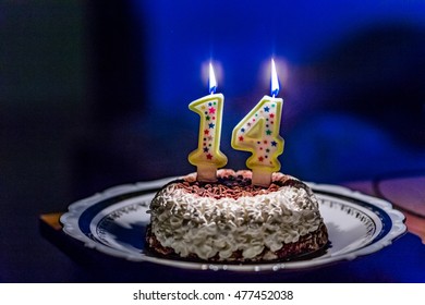 cream and chocolate cake with lit number one and number four candles to celebrate fourteen years birthday in dark blurred background