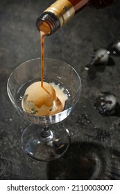 Cream Or Coffee Liqueur Pouring Into Floating High Glass With Round Ice Cube On Black Table. Copy Space.