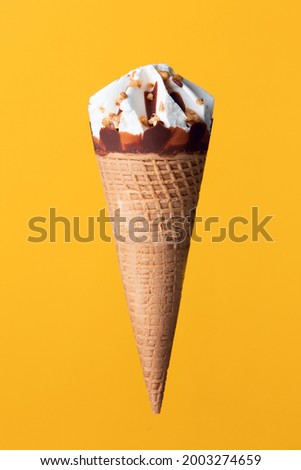Cream ice cream cone with hazelnut and almond on a yellow-orange background