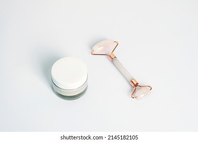 Cream In A Jar And Crystal Rose Quartz Facial Roller On White Background, Top View.