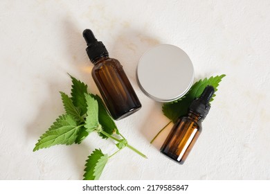cream jar two amber Glass dropper bottles of nettle oil or serum and nettle leaves beige background top view opy space nettle benefits for skin, natural cosmetics concept