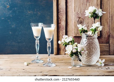 Cream liqueur and flowering branches of an apple tree on a wooden table.