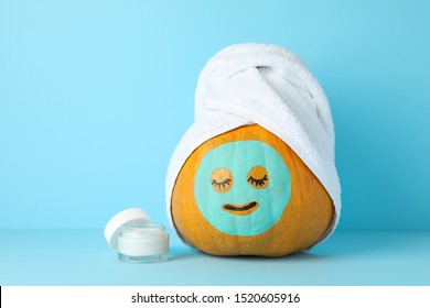 Cream, pumpkin with facial mask and towel on blue background, copy space
